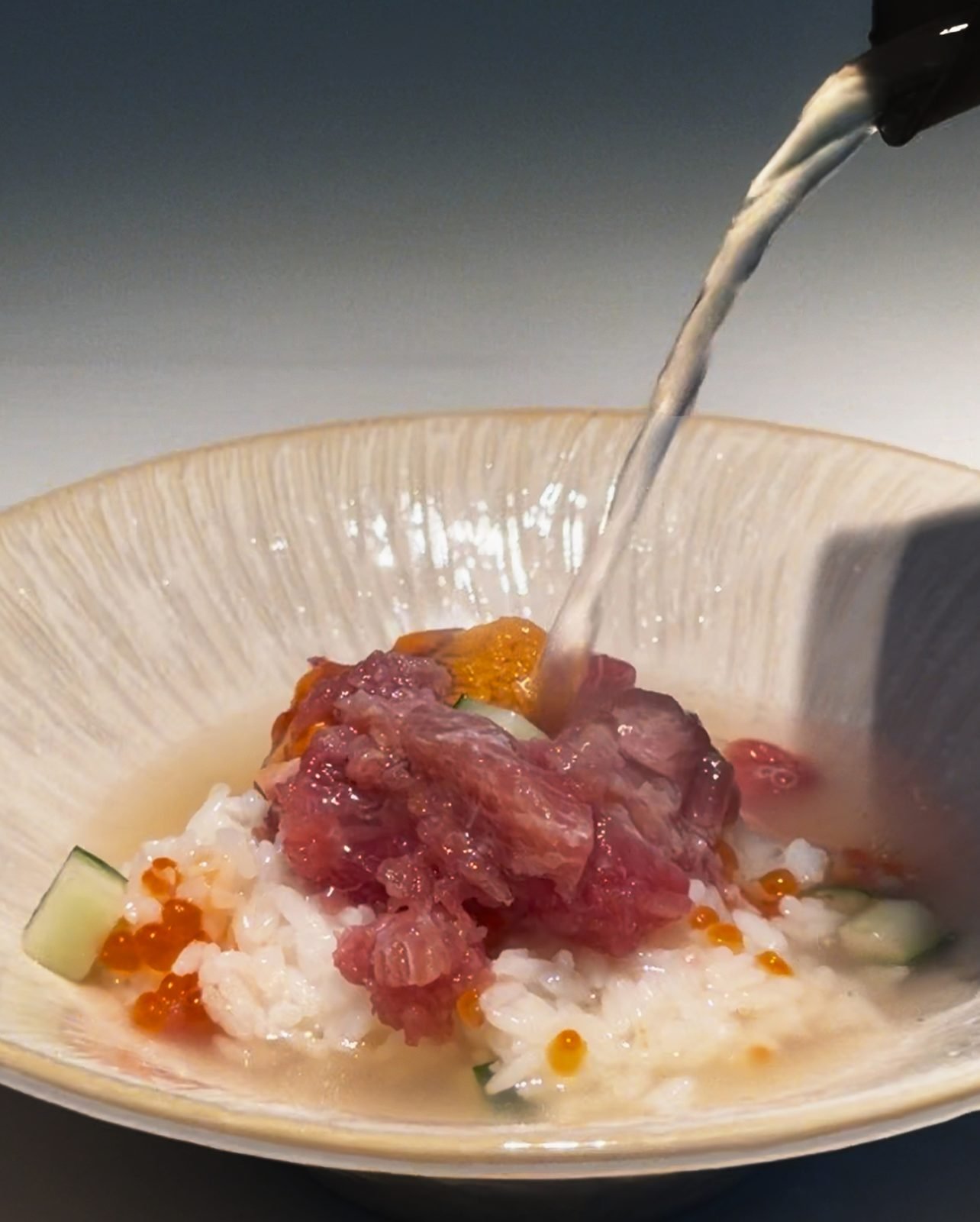 Hot dashi broth being poured over rice and seafood